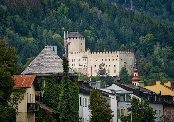 Eine mittelalterliche Burg vor bewaldeten Bergen und Häusern einer Kleinstadt.